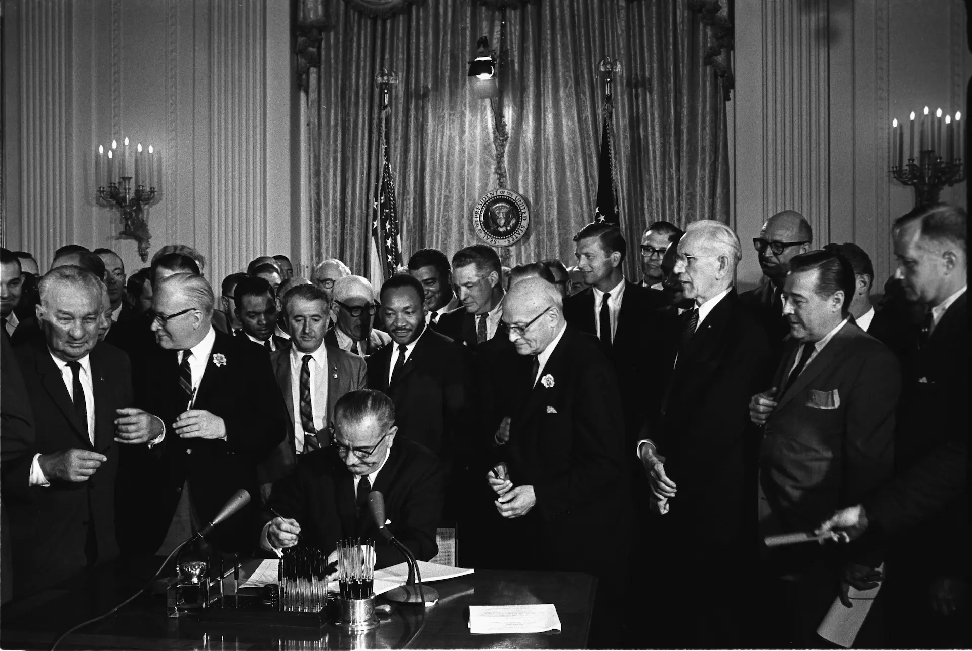 Photo of President Lyndon B. Johnson signs the Civil Rights Act of 1964. Among the guests behind him is Martin Luther King Jr.